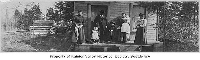 Old fashioned photo of the first family to move into Lakewood standing on the porch of their simple wood house.